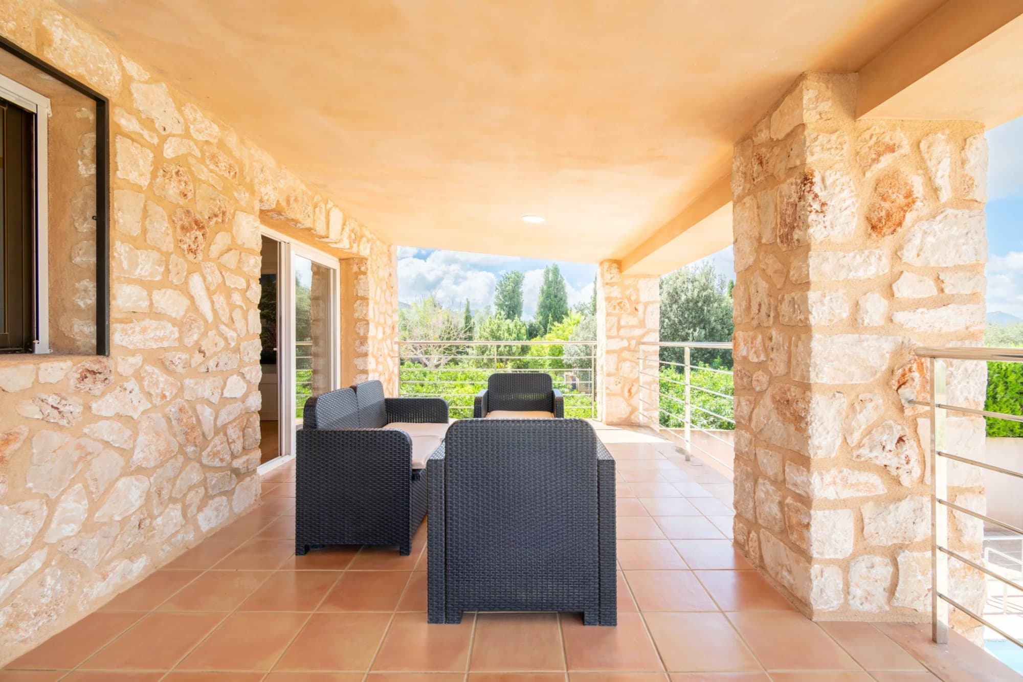 A stone-walled patio with a table and chairs, a glass door, and a view of greenery.