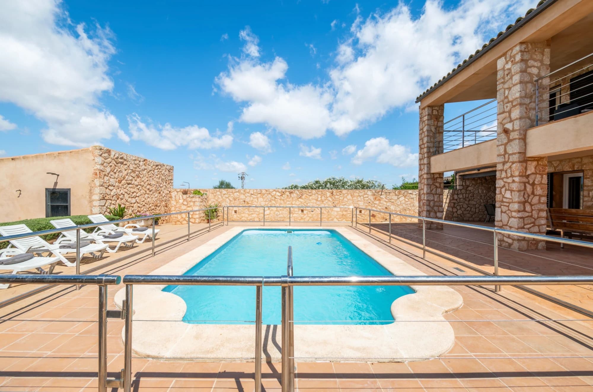 A swimming pool with lounge chairs, stone walls, and a clear sky.