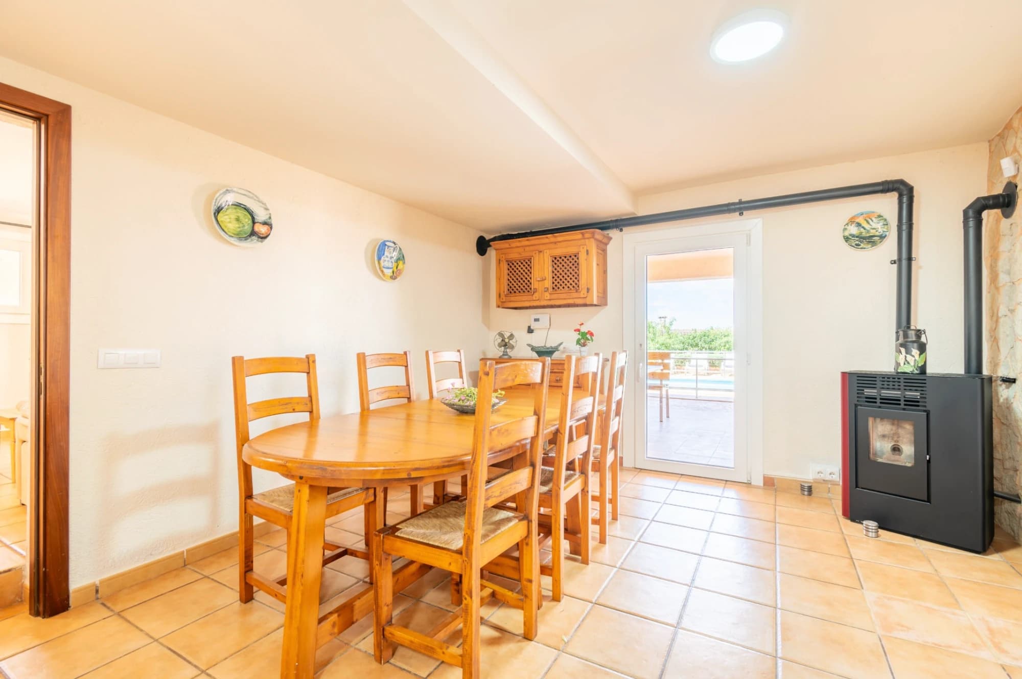A dining area with a wooden table and chairs, a black stove, and a door leading outside.