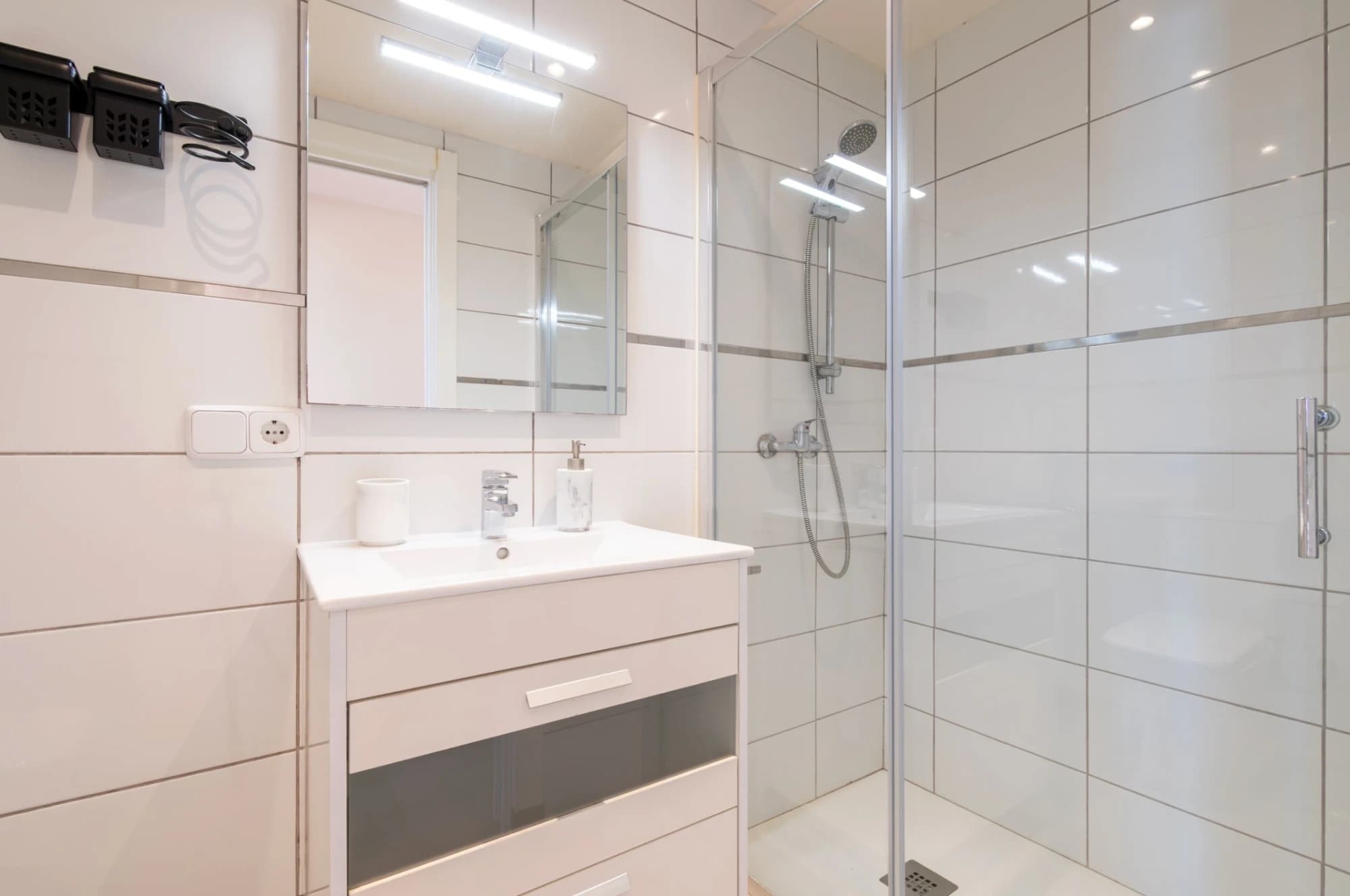 A modern bathroom with a glass shower enclosure, a white sink with a mirror, and a towel rack.